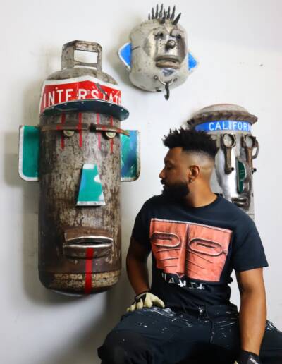 Zulu Heru sits in profile beside his sculptures